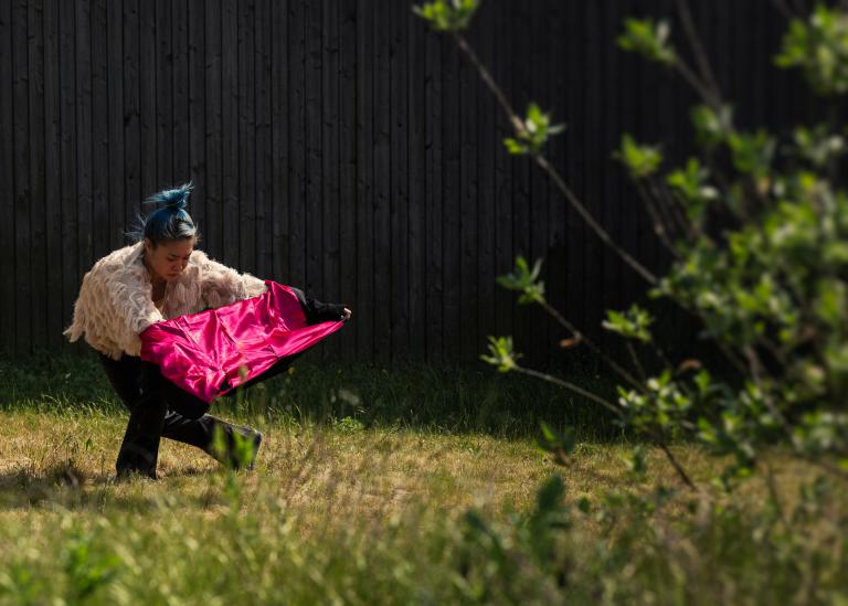 Dansaren Kat Nakui på en gräsmatta spänner ut insidan av en svart kavaj med rosa foder mellan sina utsträckta armar.