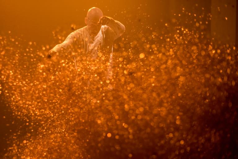 En dansare dansar bland rostfärgat glitter som virvlar i luften.