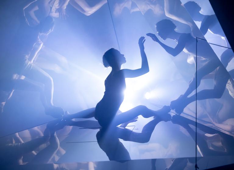 En sitter dansare i ett kalejdoskop som multiplicerar reflektioner av hennes kropp.