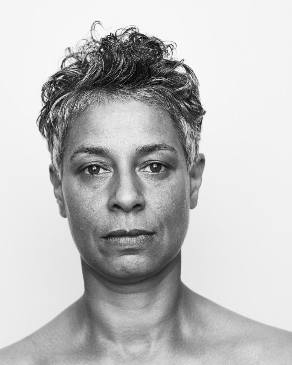 En svartvit porträttbild på dansaren och koreografen Maria Naidu med kort, lite lockigt svart-grått hår.