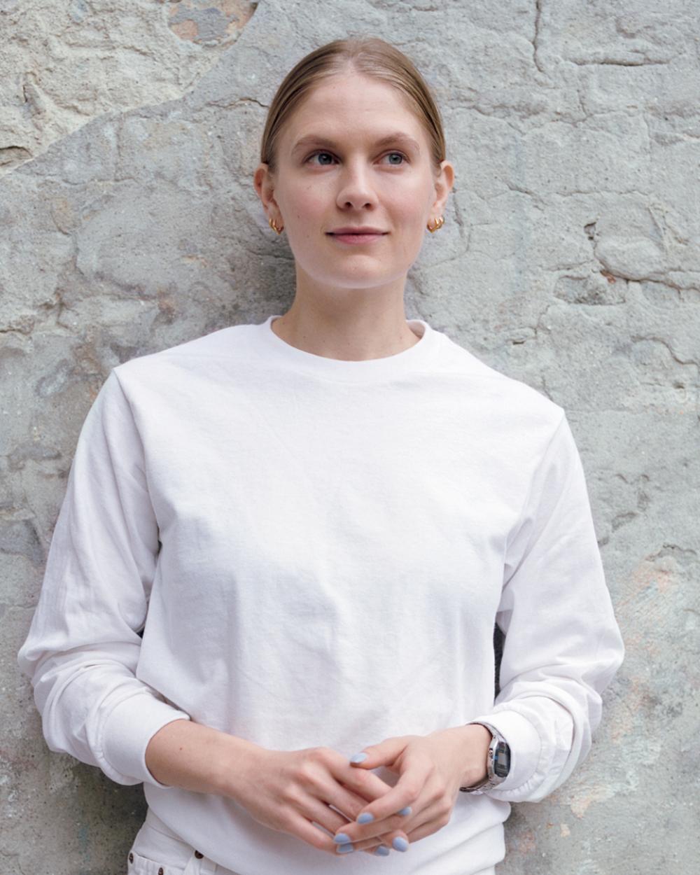 Emma Holten lutar sig mot en stenvägg klädd i vit tröja.