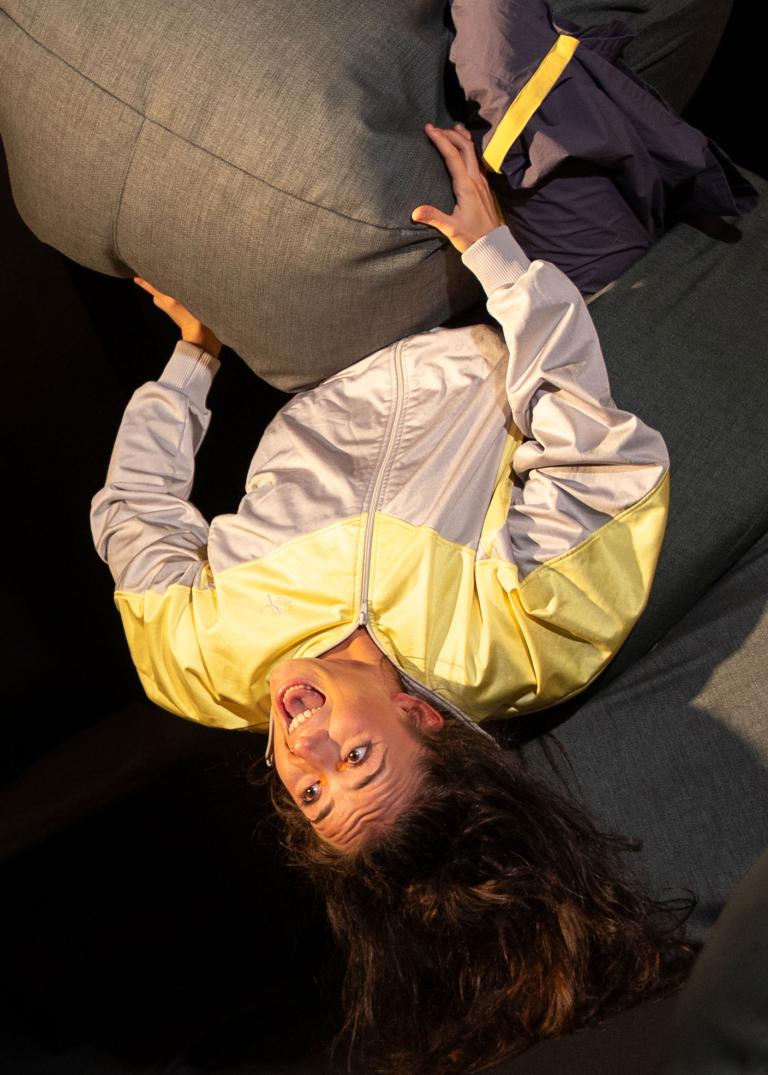 Skånes Dansteaters dansare Valentina Messieri, sitter bland flera grå sittpuffar och lutar sig bakåt så att det ser ut som att hon faller baklänges.