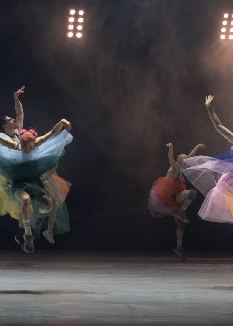 Femton dansare gör stora danssprång genom luften klädda i tyllkjola i regnbågens alla färger i Skånes Dansteaters jubileumsföreställning Wing Ding av  koreografen Lidia Wos.