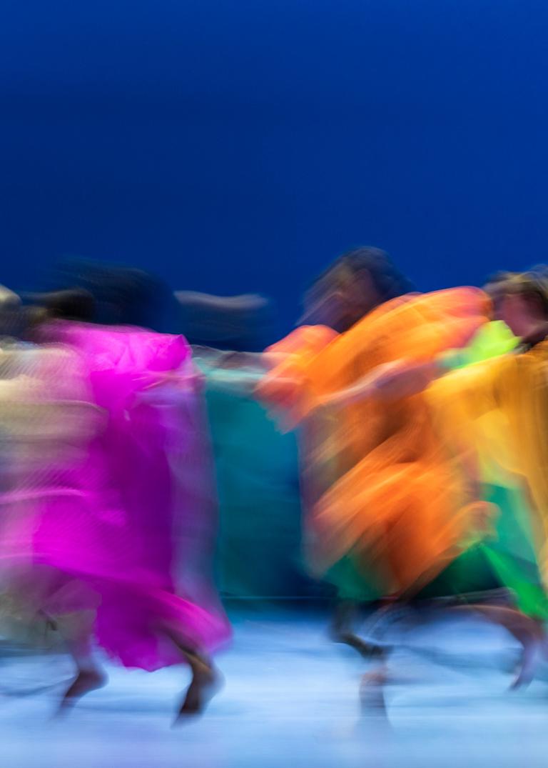 Dansare klädda i lätt genomskinliga fladdriga dräkter i starka färger springer i en ring i Skånes Dansteaters dansföreställning Out of the Blue på Malmö Opera.