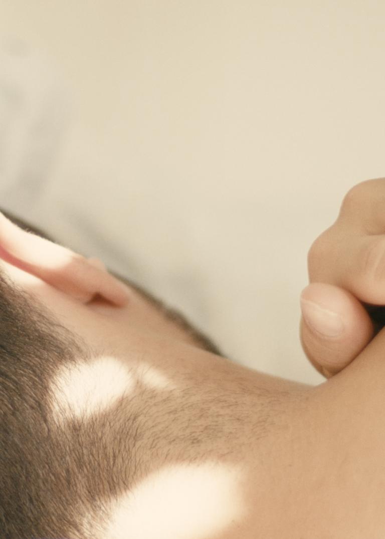 En person med mörkt kort hår ligger på sidan med ryggen mot dig och en hand på axeln i Madeleine Månssons dansfilm Preface.