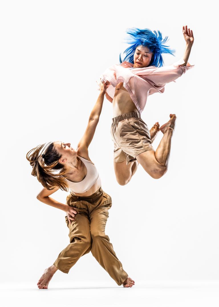 Dansaren Hanna hukar och sträcker sig upp mot dansaren Kat som hoppar högt upp i luften.