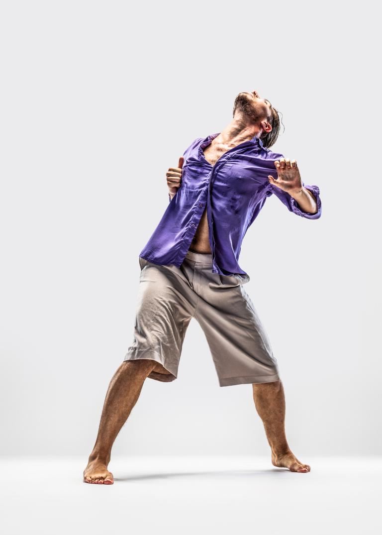 Dansaren Fabrizio di Franco sträcker sig bakåt och uppåt, klädd i ljusa shorts och en lila skjorta.