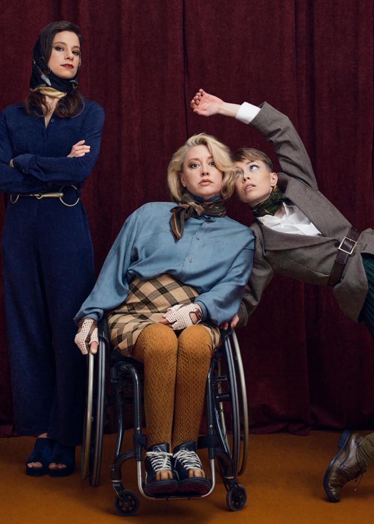 Dansarna Marion, Madeleine och Emma står framför ett mörkrött draperi vid ett bord med ett tänt ljus och en skål med äpplen.