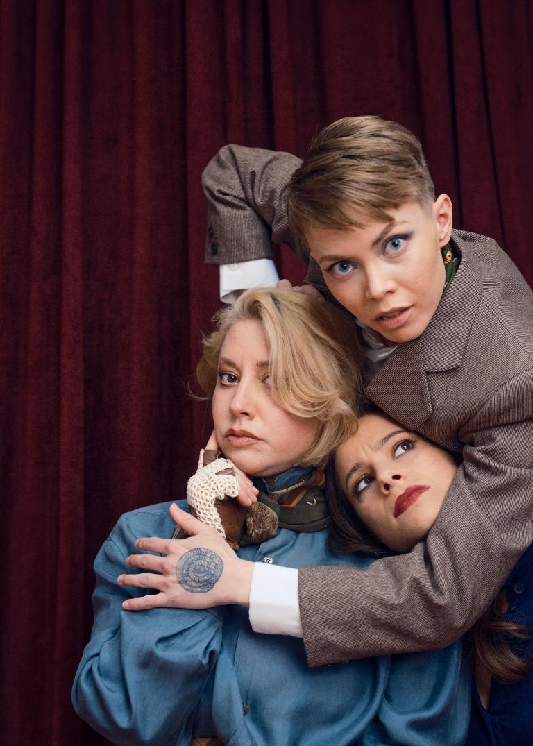 Dansaren Emma håller om dansarna Madeleine och Marion. Madeleine ser fundersam ut och Marion tittar misstänksamt på Emma.