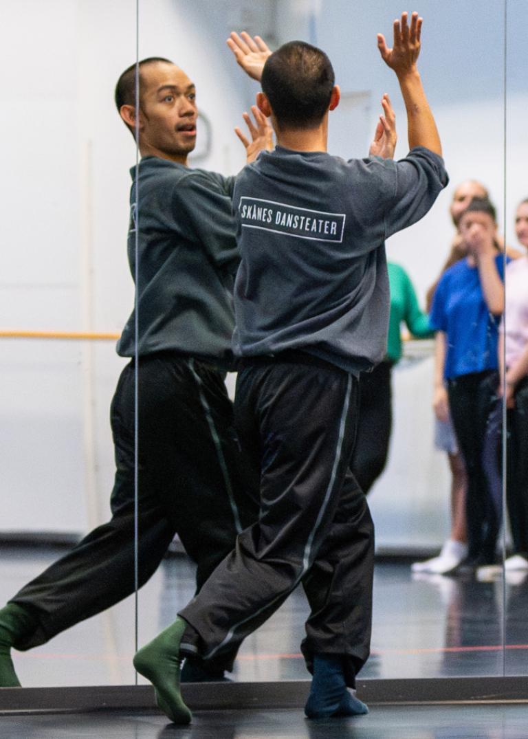 Dansaren Michael visar dansrörelser framför en spegel för workshopdeltagare tillsammans med teckenspråkstolk i Skånes Dansteaters dansstudio.