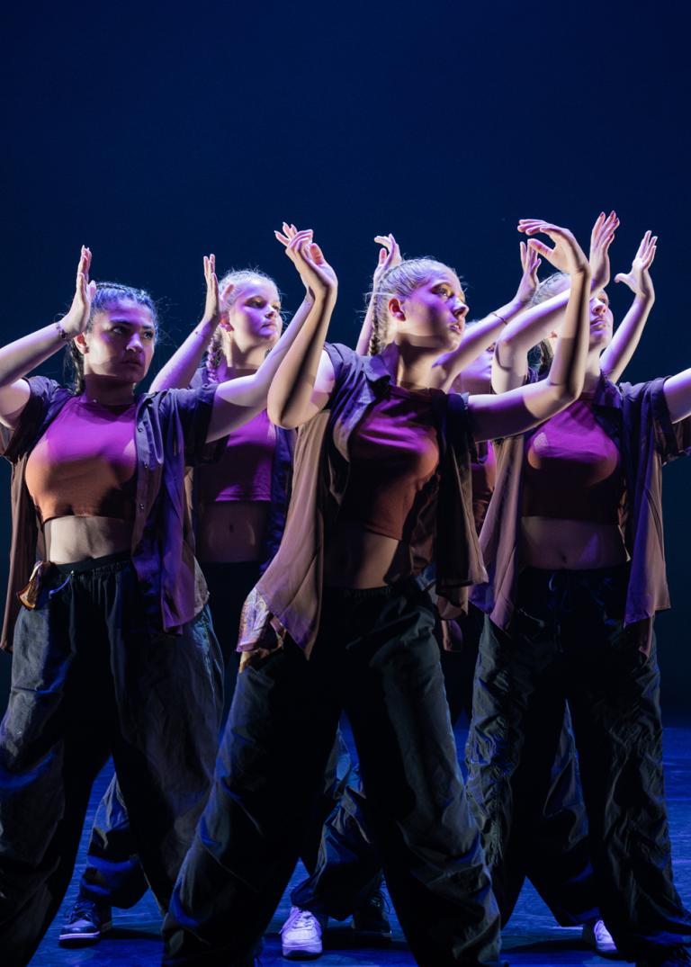 Unga dansare står tätt ihop med armarna i vinkel framför sig.