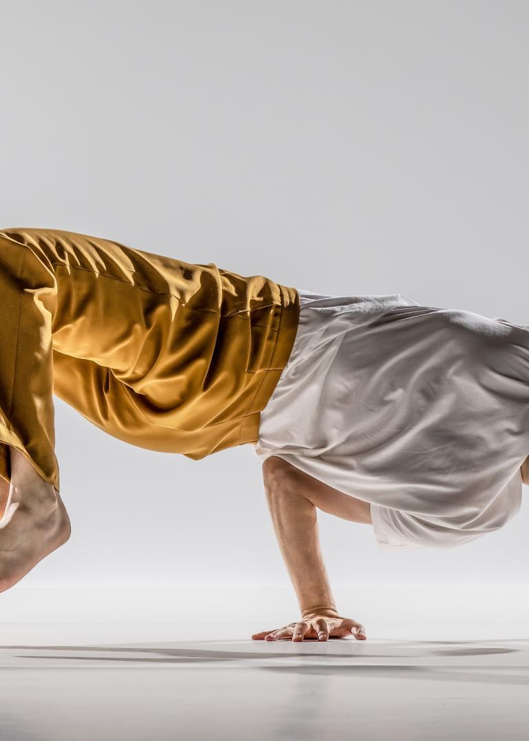 Dansaren Samuel Denton i mörkgula byxor och vit tshirt balanserar på en hand.