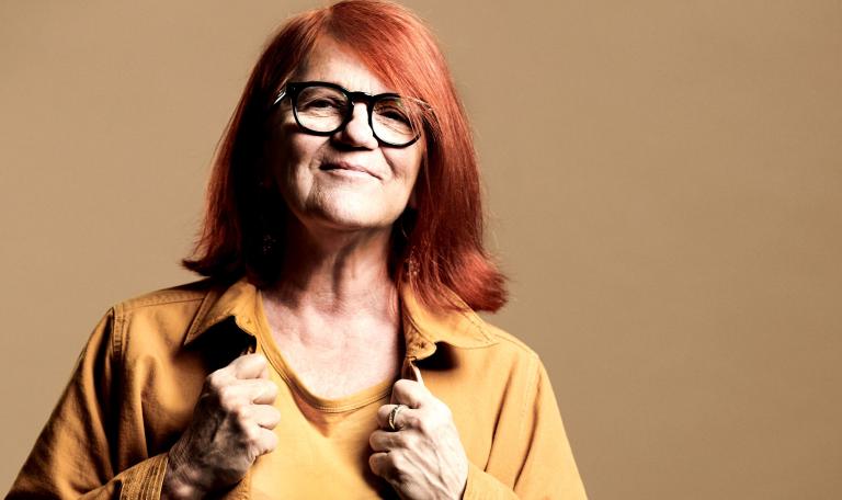 Gudrun Hauksdottir med rött halvlångt hår, gult linne och skjorta och glasögon med svarta bågar.