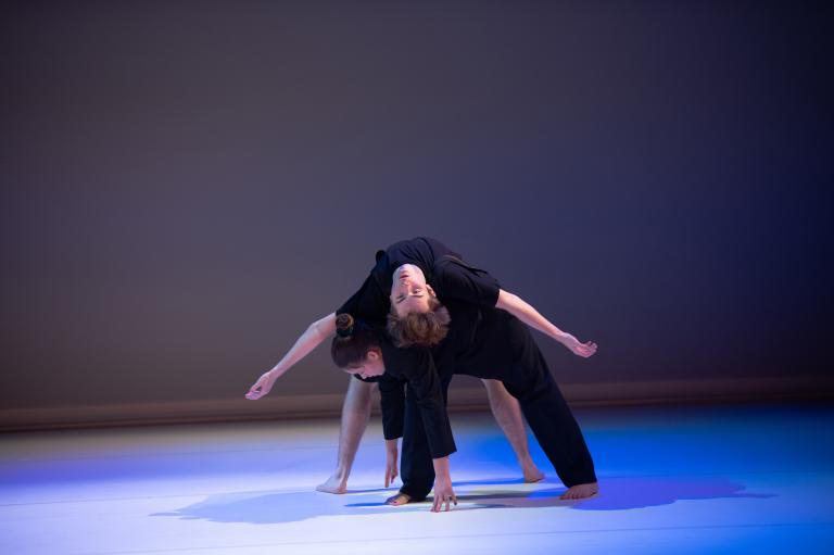 En dansare ligger på rygg böjd över ryggen på en annan dansare.