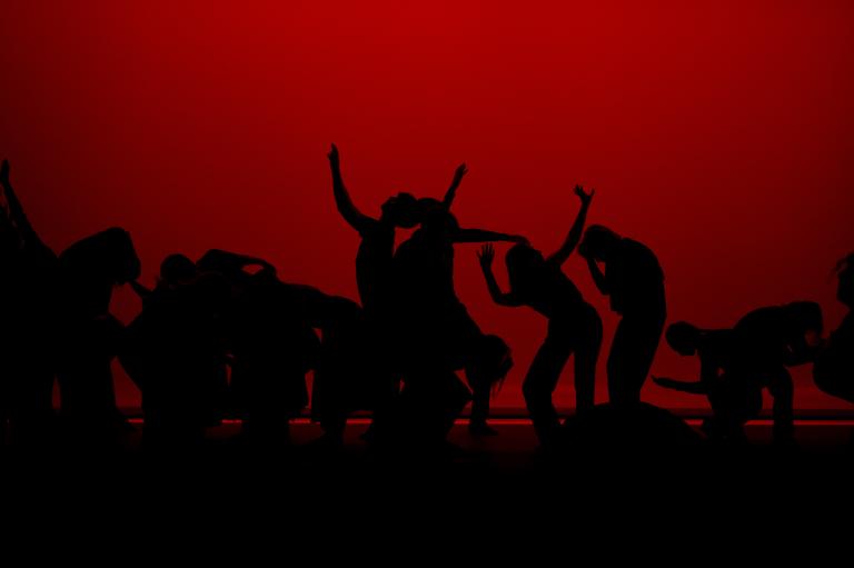 Ett stort antal dansare i siluett mot en röd vägg.