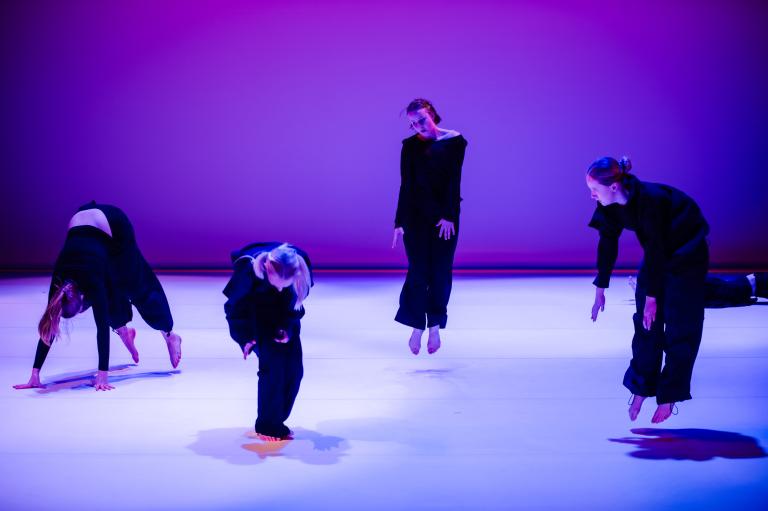 Fyra dansare i svarta kläder böjer sig ner mot golvet eller hoppar böjda upp i luften.