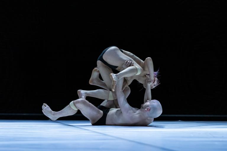 Dansaren Samuel Denton ligger på rygg på golvet och balanserar dansaren Kat Nakui på sina händer och knän.