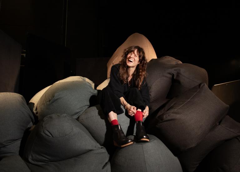 Koreografen Heidi Vierthaler sitter på en stor hög grå sittpuffar och skrattar.