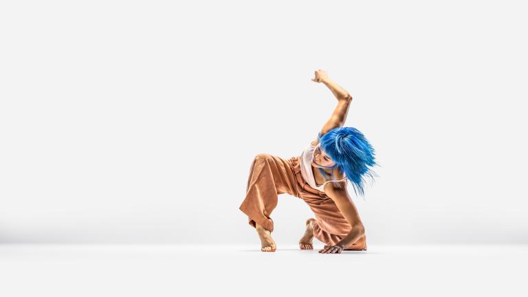 Skånes Dansteaters dansre Kat lutar sig på vänter knä och armbåge medan hon står på tå med andra foten och stråcker andra armen uppåt.