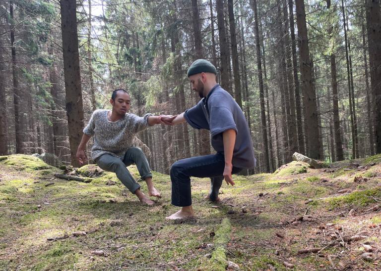 Dansarna Michael Marquez och Samuel Denton håller varandra i en hand medan de sträcker sig från varandra i skogen under inspelningen av Skånes Dansteaters dansfilm Once in the Forest.