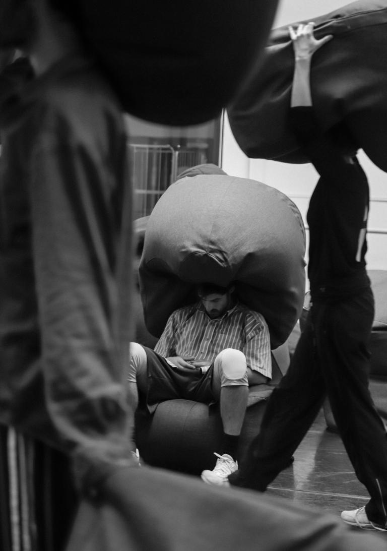 Dansaren Kit sitter på en sittpuff med en sittpuff på huvudet medan två andra dansare går framför honom med sittpuffar på sina huvuden. Repetitioner av Skånes Dansteaters familjeföreställning Myller av koreograf Heidi Vierthaler.