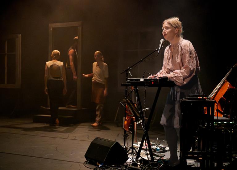 Musikern Emma spelar keyboard och sjunger i dansföreställningen Inner SOng medan dansarna går ut genom en dörröppning i bakgrunden.