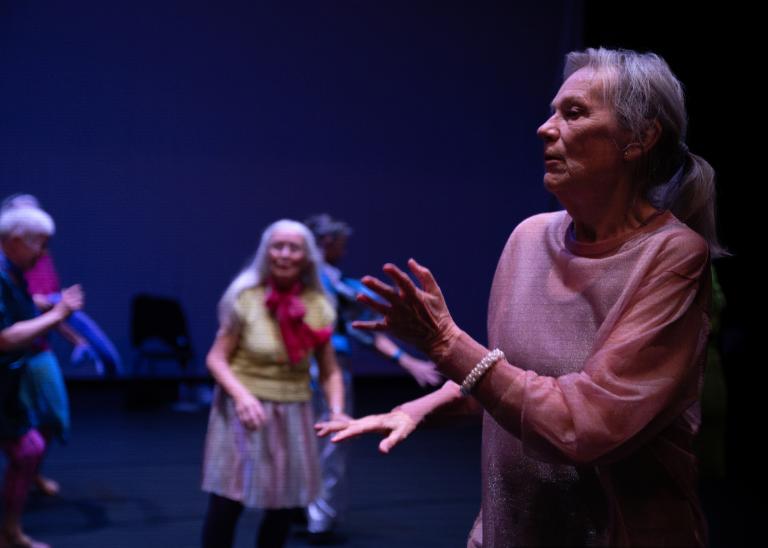 En gästdansare över 60 år med håret i hästsvans, klädd i en skir ljusrosa topp, dansar med armar och händer framför sig i dansföreställningen Jag minns mig själv.