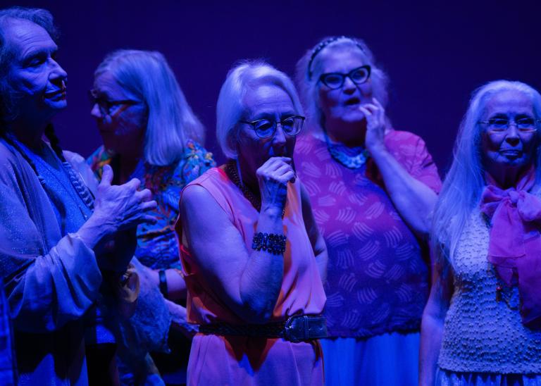 Gästdansare över 60 år står i en grupp i blått ljus. De ser eftertänksamma ut.