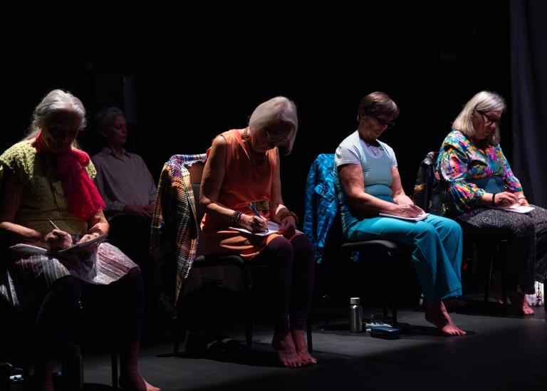 Fyra gästdansare sitter på stolar på scen och skriver i anteckningsböcker i dansföreställningen Jag minns mig själv.