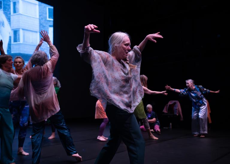 Gästdansare dansar tillsammans med armarna böjda ovanför sig framför en projektionsduk som visar en bild från förr i dansföreställningen Jag minns mig själv.