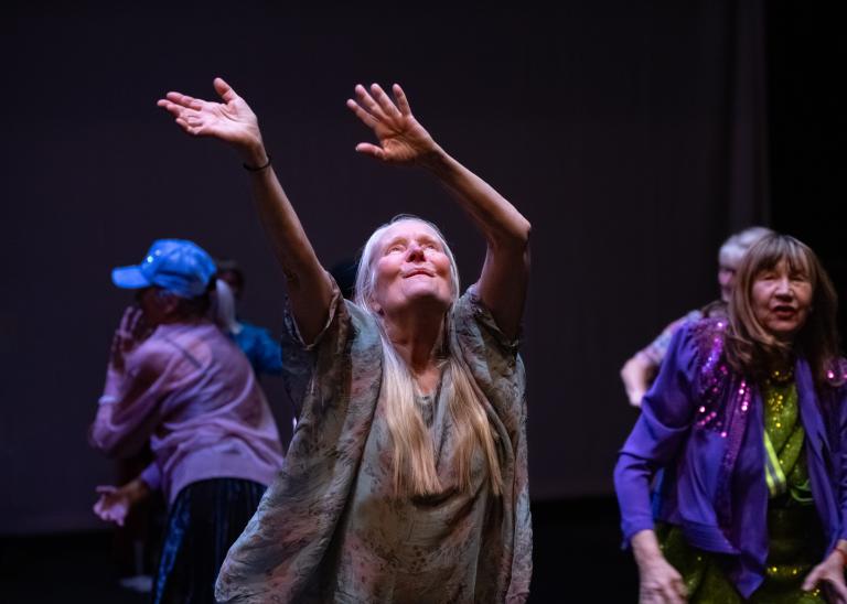 En gästdansare över 60 år klädd i en skir tunika dansar med armarna svepandes högt i luften framför sig i dansföreställningen Jag minns mig själv.