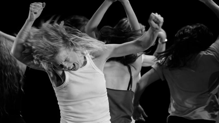 En svartvit bild av personer som dansar vilt klädda i linnen med armarna svingandes upp i luften.