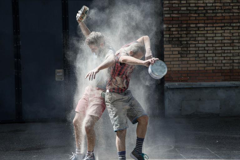 Två dansare i rutiga skjortor och shorts dansar i ett dammoln. 