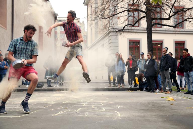 Två dansare studsar runt ovanför en lekhage på en gata och kastar damm på varandra.