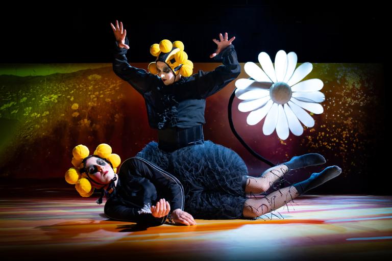 En dansare håller upp armarna i luften och sitter på en annan dansare som ligger på golvet. 