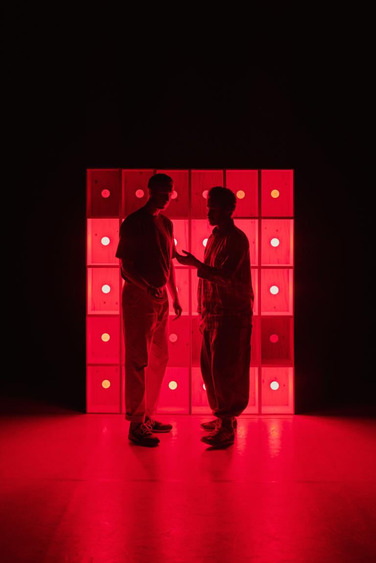 Dansarna Viktor och Yared pratar tillsammans framför en lysande röd vägg.