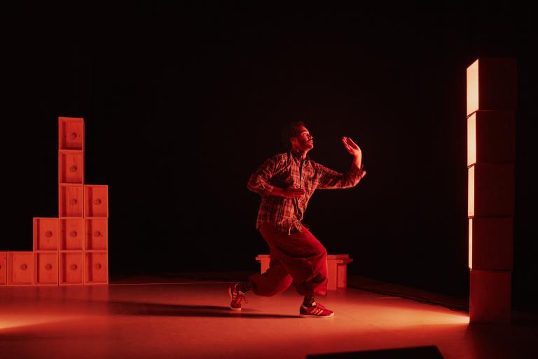 Dansaren Yared dansar mot ljuset på en rödbelyst scen.