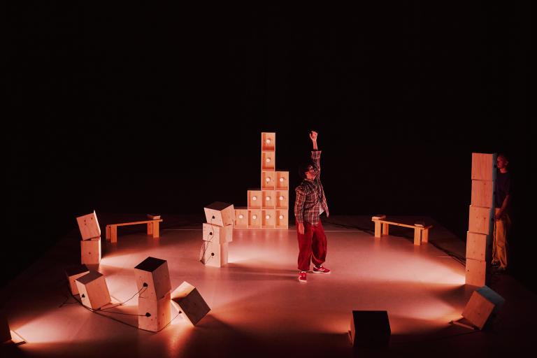 Dansaren Yared står på en svagt belyst scen bland staplar av omålade trälådor i olika höjder.