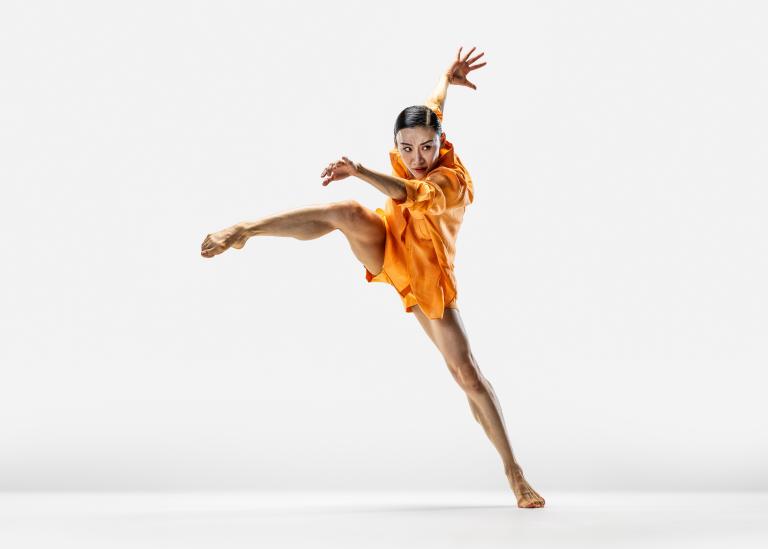 Dansaren Jing Yi Wang tar ett stort steg i sidled med armarna svängande framför och bakom sig.