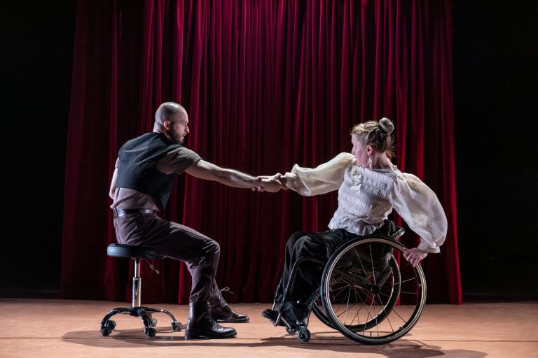 Dansarna Tomáš och Madeleine håller varandra i en arm mitt emot varandra. De rör sig snurrandes en på en pall med hjul och en i rullstol.