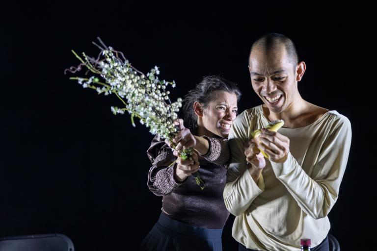 Dansaren Michael skalar en banan med ett stort leende. Bakom honom tar Marion sats för att slå honom med en stor bukett späda vita blommor.