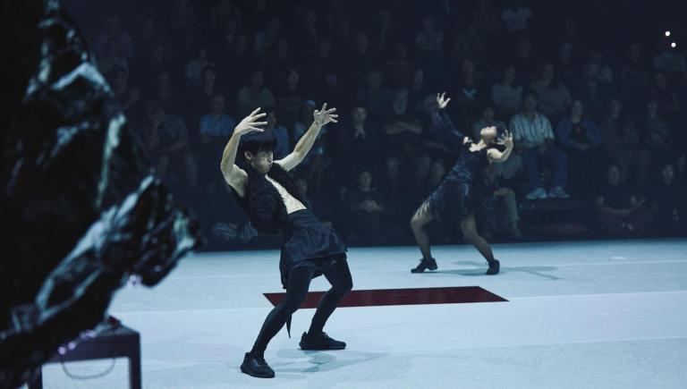 Dansare i åtsittande svarta käder böjer sig baklänges med armar och ben utsträckta längs sidorna. 