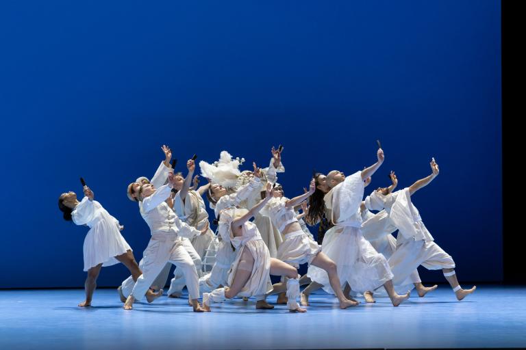 Dansare klädda i vita historiska kläder dansar synkroniserat tillsammans i ett blått scenrum.