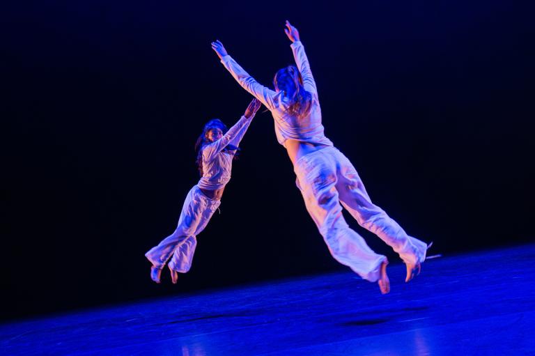 Två dansare gör stora danshopp mot varandra som om de flyger mot varandra.