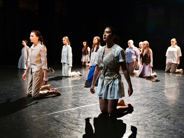 Danselever från malmö Kulturskola står på knä klädda i ljusa kläder med allvarliga ansikten.