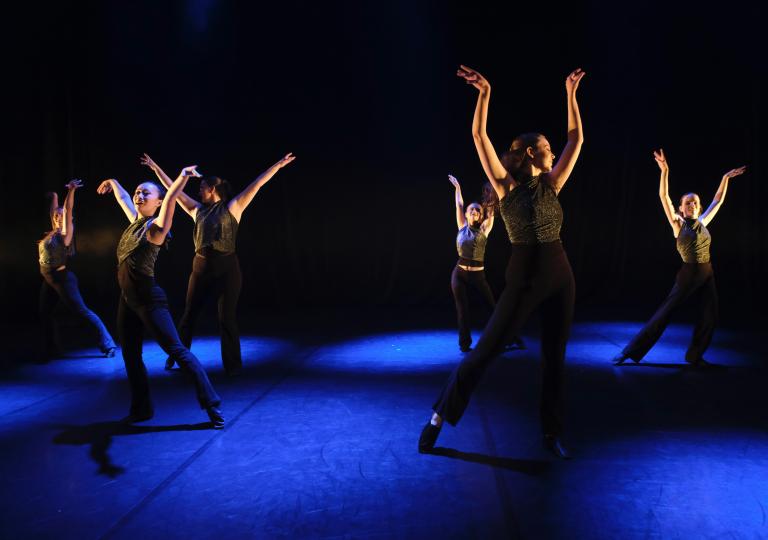 Danselever från Malmö Kulturskola dansar på en blåskimrande scen i tights och linnen med armarna uppsträckta.