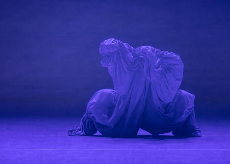 En dansare täckt i skimrande blått tyg står bredbent i Skånes Dansteaters dansföreställning Out of the Blue.