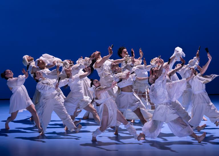Dansare klädda i vita kläder med olika historiska detaljer i ett stort steg med blicken uppåt i Skånes Dansteaters dansföreställning Out of the Blue.