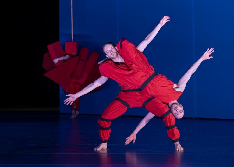 Dansaren Samuel Denton hänger i knäna på dansaren Jure Gostinčars axlar. De lutar på diagonalen och sträcker ut sina armar i Skånes Dansteaters dansföreställning Out of the Blue.
