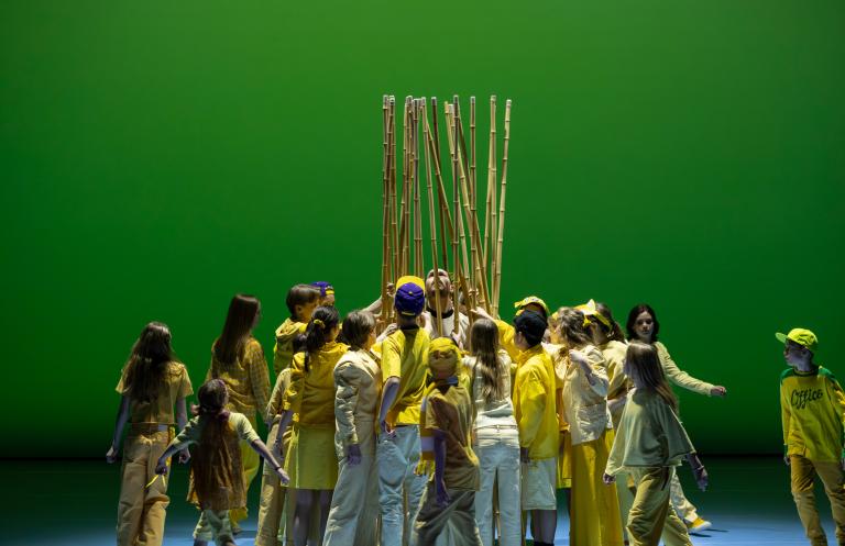 MAlmö Operas barnkör klädda i gula kläder omringar dansaren Fabrizio di Franco med långa träpinnar i Skånes Dansteaters dansföreställning Out of the Blue.